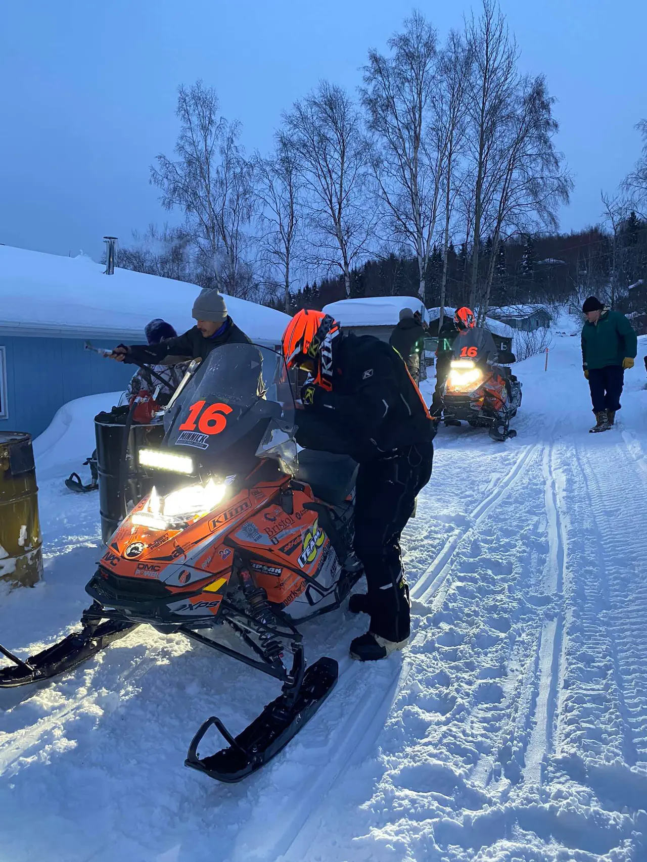 Team 16 stopped at the Ruby checkpoint in blue morning light, crew around the machine and the trail running away between the trees.