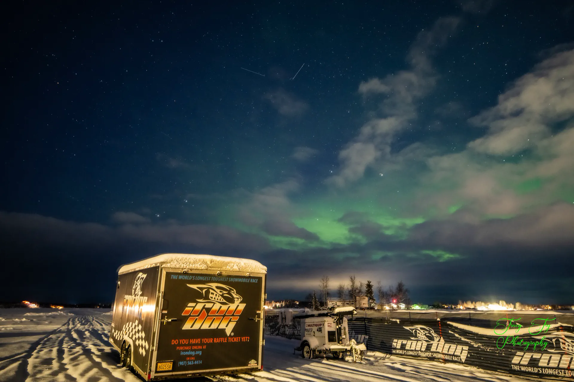 An Iron Dog equipment trailer parked out on the lake ice under the aurora before the start.
