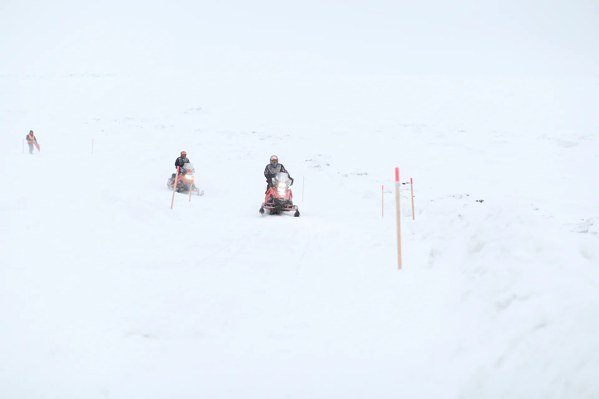 Racers reduced to specks on a vast open snowfield, a single trail marker in the foreground.