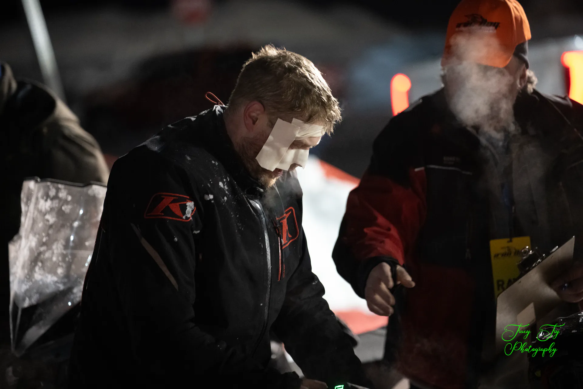 A racer whose face is white with frost stands in the dark beside a man whose beard is caked solid with ice.