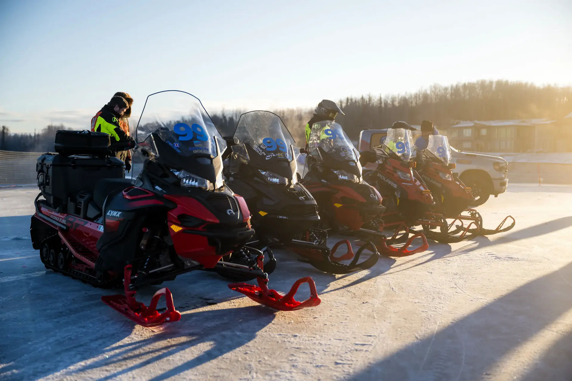 Ambassador Class sleds lined up nose to tail on the lake ice in low sunrise light.
